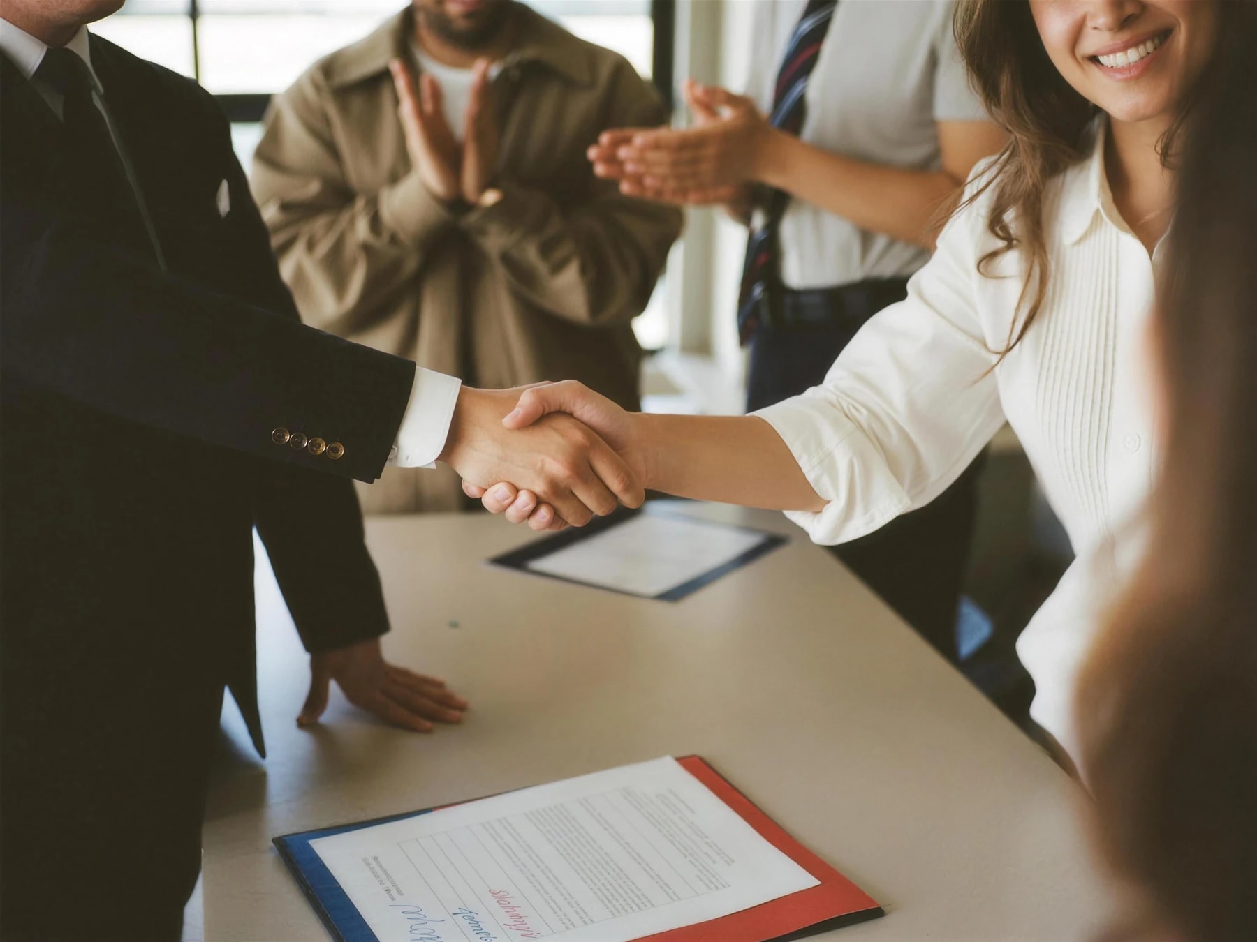 Poignée de main au-dessus d'une convention signée, sous les applaudissements de quelques étudiants.