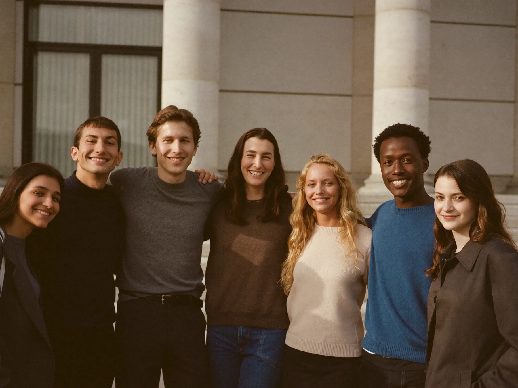 Un groupe d'étudiantes et d'étudiants souriants, réunis devant l'entrée de leur école.