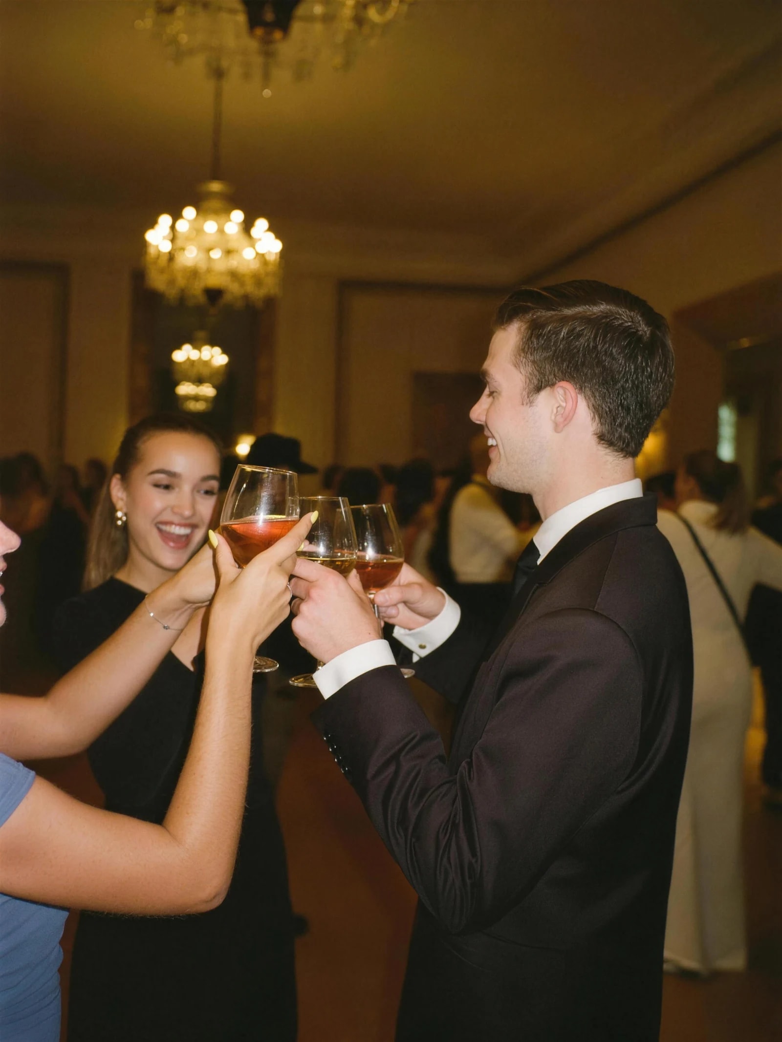 Des étudiantes et des étudiants en tenue de soirée trinquent lors d'un gala, sous les lustres d'une salle de réception.