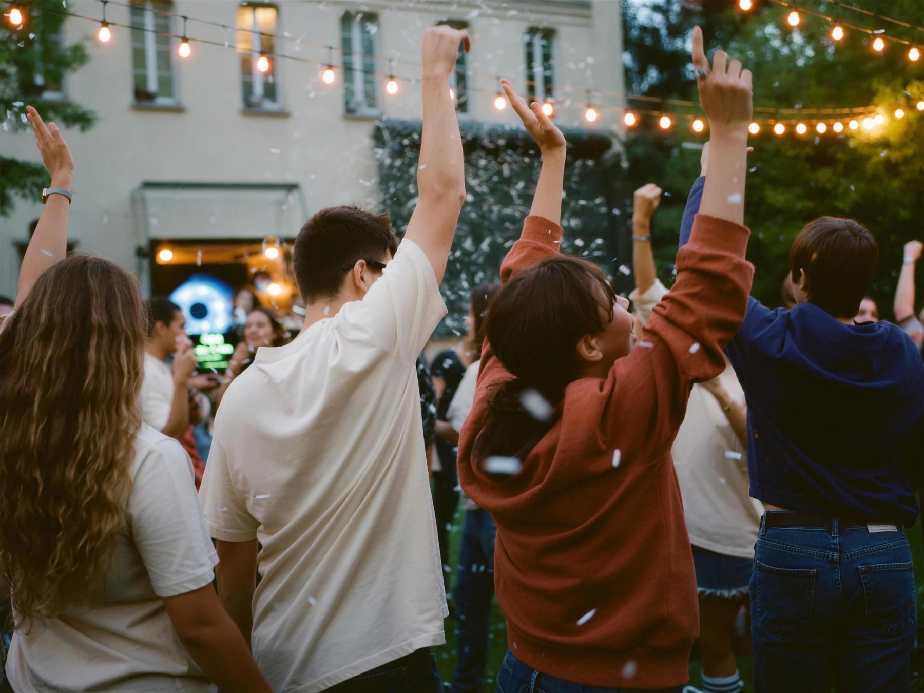 Des étudiants dansent bras levés sous des guirlandes lumineuses, confettis en suspension, lors d'une soirée d'intégration.